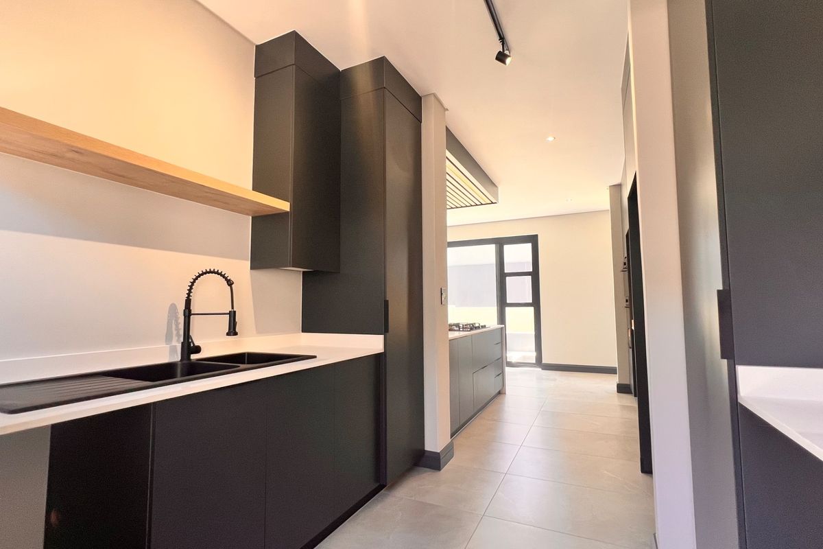 Modern kitchen featuring sleek matte black cabinetry, stone countertops, a black undermount sink with gooseneck tap, and minimalist floating timber shelving.