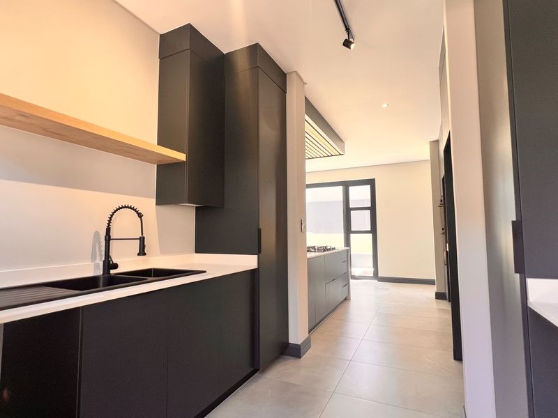 Modern kitchen featuring sleek matte black cabinetry, stone countertops, a black undermount sink with gooseneck tap, and minimalist floating timber shelving.