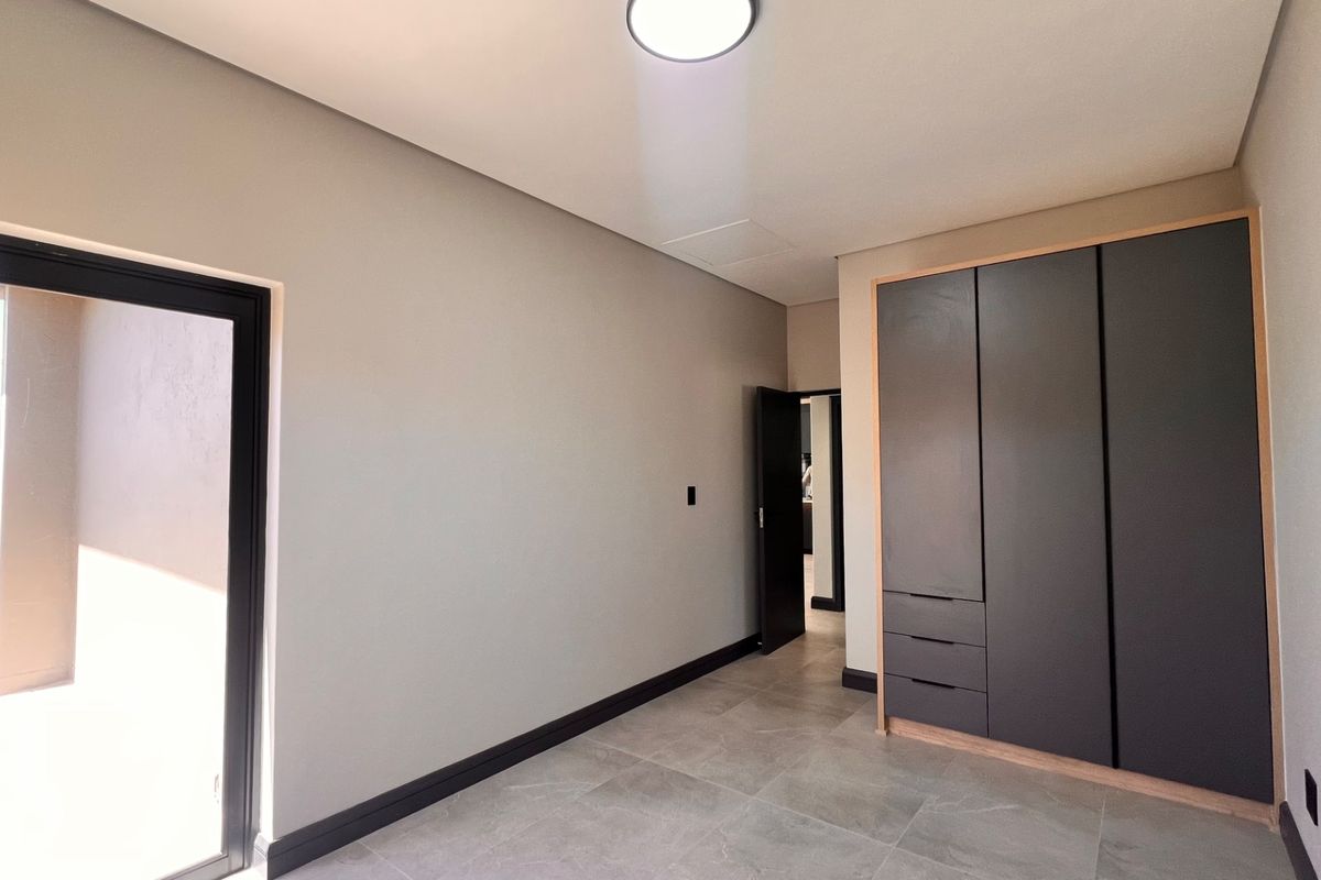 A modern, empty bedroom featuring neutral walls, tiled flooring, and sleek built-in cupboards with direct access to an outdoor area.