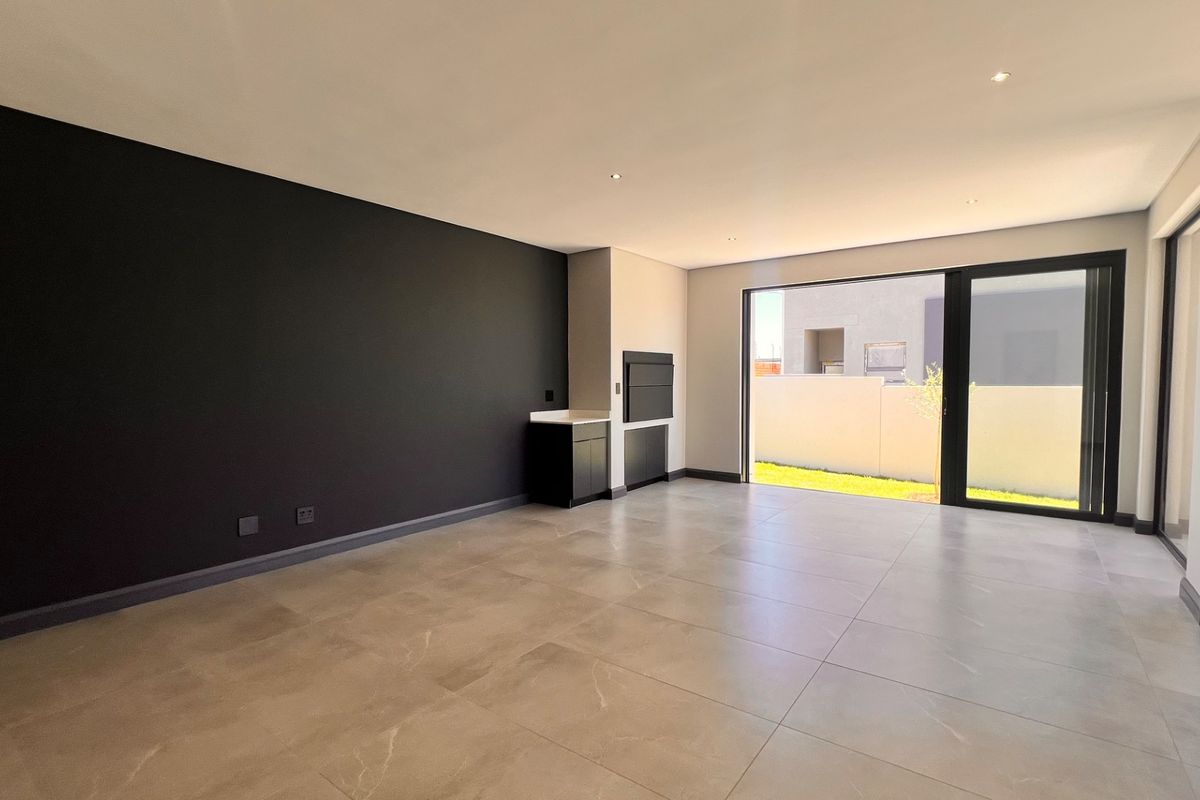 Spacious open-plan living area featuring large format floor tiles, a modern built-in braai, and sliding glass doors leading to the garden.
