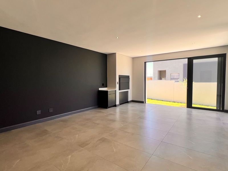 Spacious open-plan living area featuring large format floor tiles, a modern built-in braai, and sliding glass doors leading to the garden.