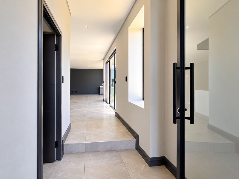 A modern, spacious hallway featuring neutral tiled flooring, recessed lighting, and clean architectural lines leading into an open-plan living area.
