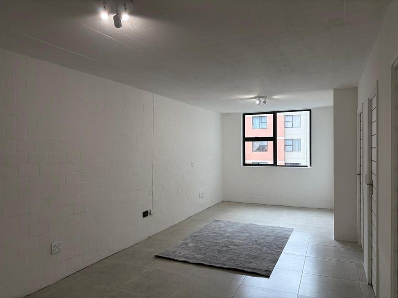 A bright, empty living room featuring tiled flooring, a painted brick feature wall, and large aluminium-framed windows.