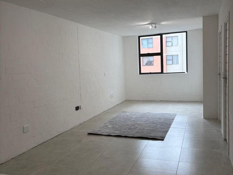 An empty open-plan living area featuring neutral tiled flooring, painted brick walls, and a large window providing natural light.