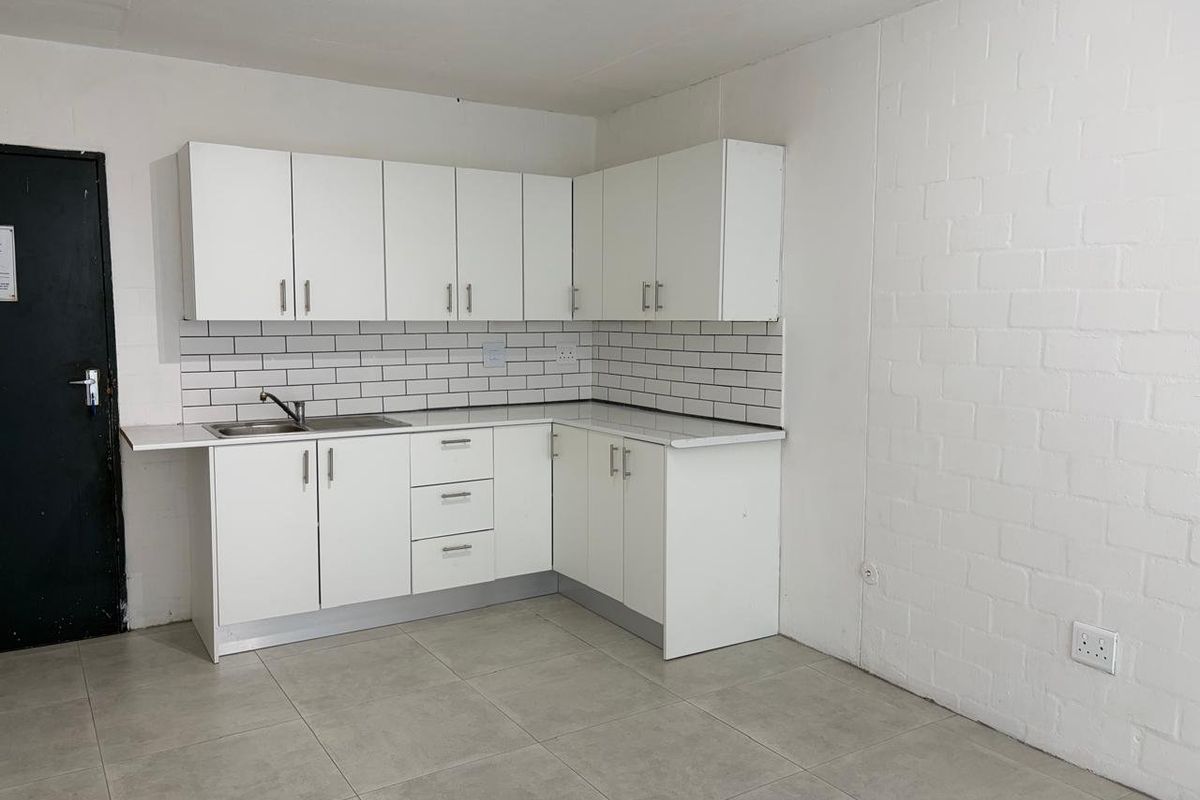 A clean, minimalist kitchen featuring white cabinetry, a subway tile backsplash, and neutral tiled flooring in an open-plan layout.