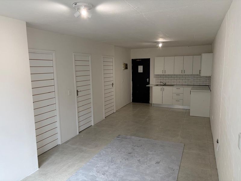 An open-plan living and kitchen area featuring tiled flooring, white cabinetry, subway tile backsplash, and multiple internal doors.