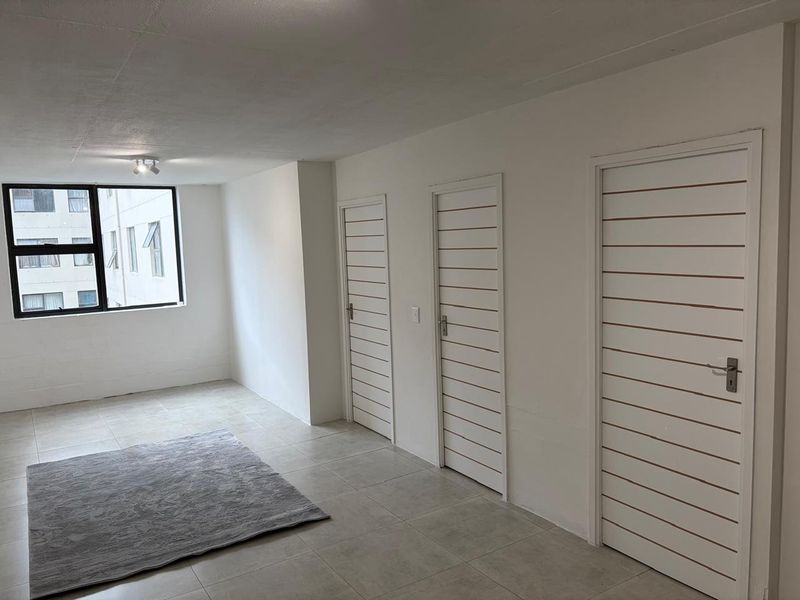 A bright, open-plan living area featuring neutral tiled flooring, clean white walls, and three internal doors leading to adjacent rooms.