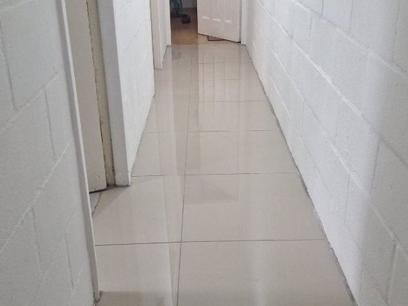 A clean, empty hallway featuring neutral tiled flooring and painted blockwork walls, providing a bright and functional transition space between rooms.