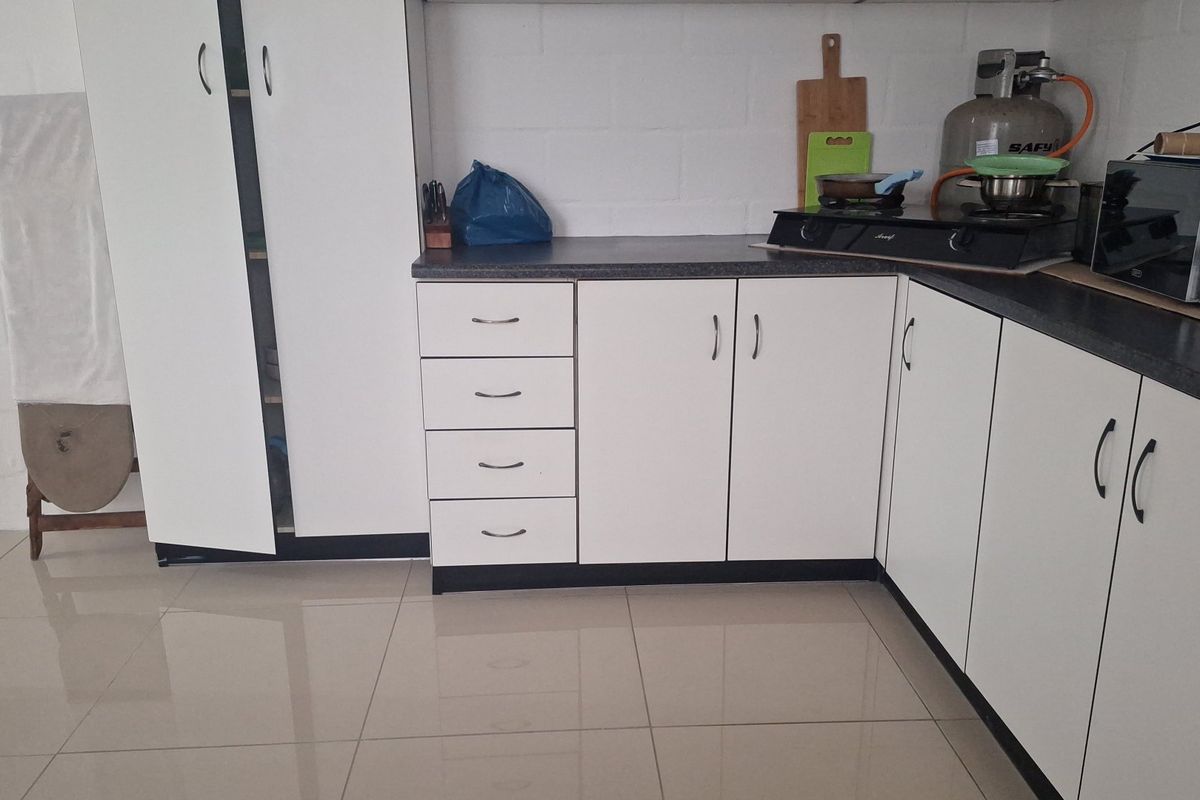 A functional kitchen area featuring white built-in cabinetry, dark laminate countertops, a gas hob, and neutral tiled flooring.