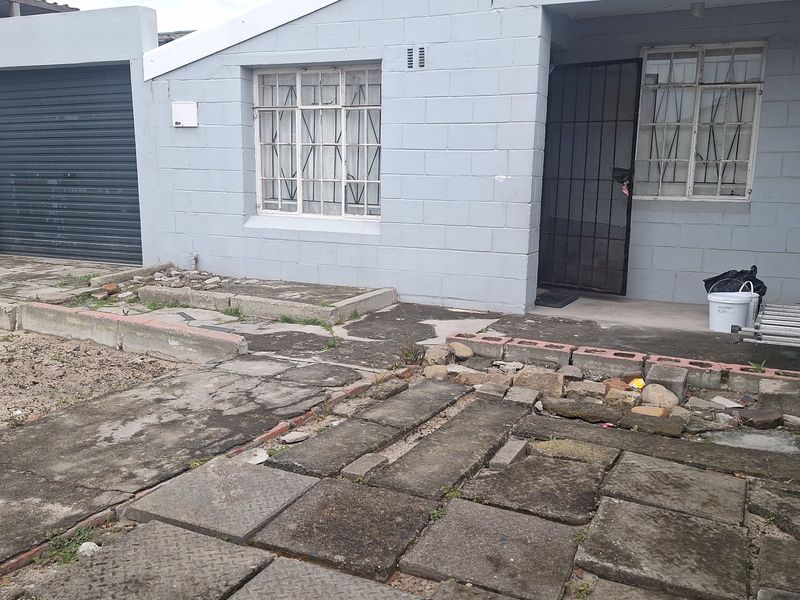 Front exterior view of the property featuring a roller shutter garage, security-fitted windows, and a paved driveway area in need of maintenance.