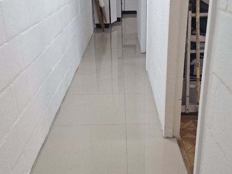 A clean, tiled hallway leading towards a kitchen area, featuring painted blockwork walls and a simple, functional layout.