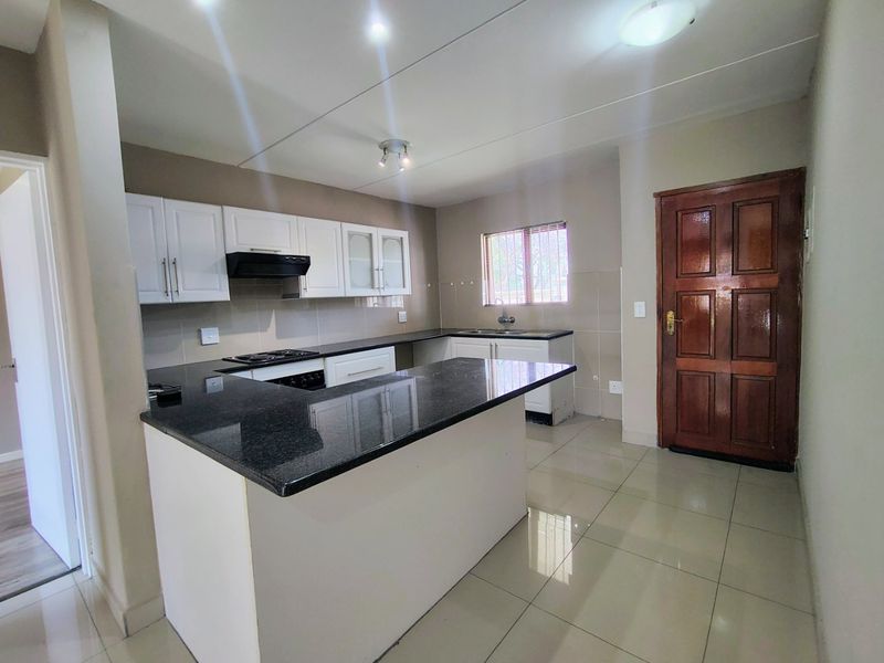 A clean, modern kitchen featuring granite countertops, white cabinetry, a built-in hob with extractor fan, and tiled flooring throughout.