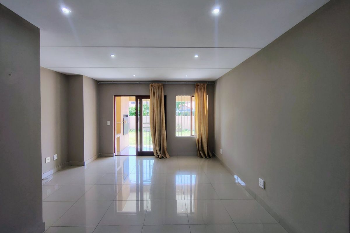 A spacious, empty living room featuring neutral tiled flooring, recessed downlighting, and direct access to an outdoor patio area through a sliding glass door.