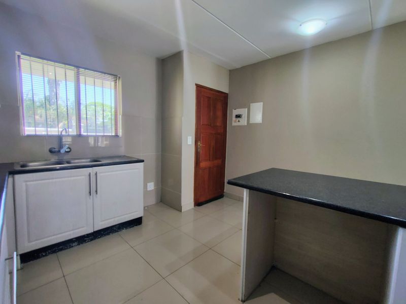 A functional kitchen featuring white cabinetry, dark granite countertops, tiled flooring, and a double sink with a window view.