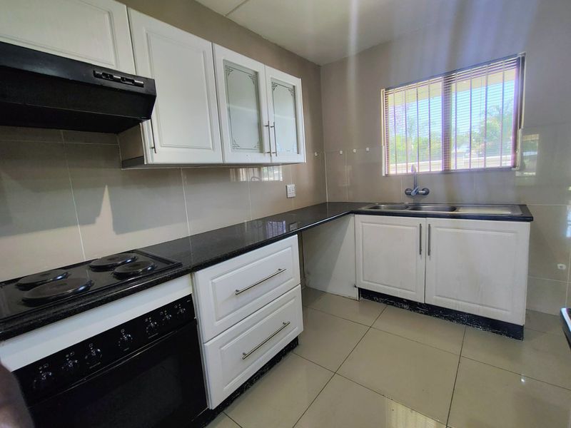A functional kitchen featuring white cabinetry, black granite countertops, a double sink, and a built-in electric stove with an extractor fan.
