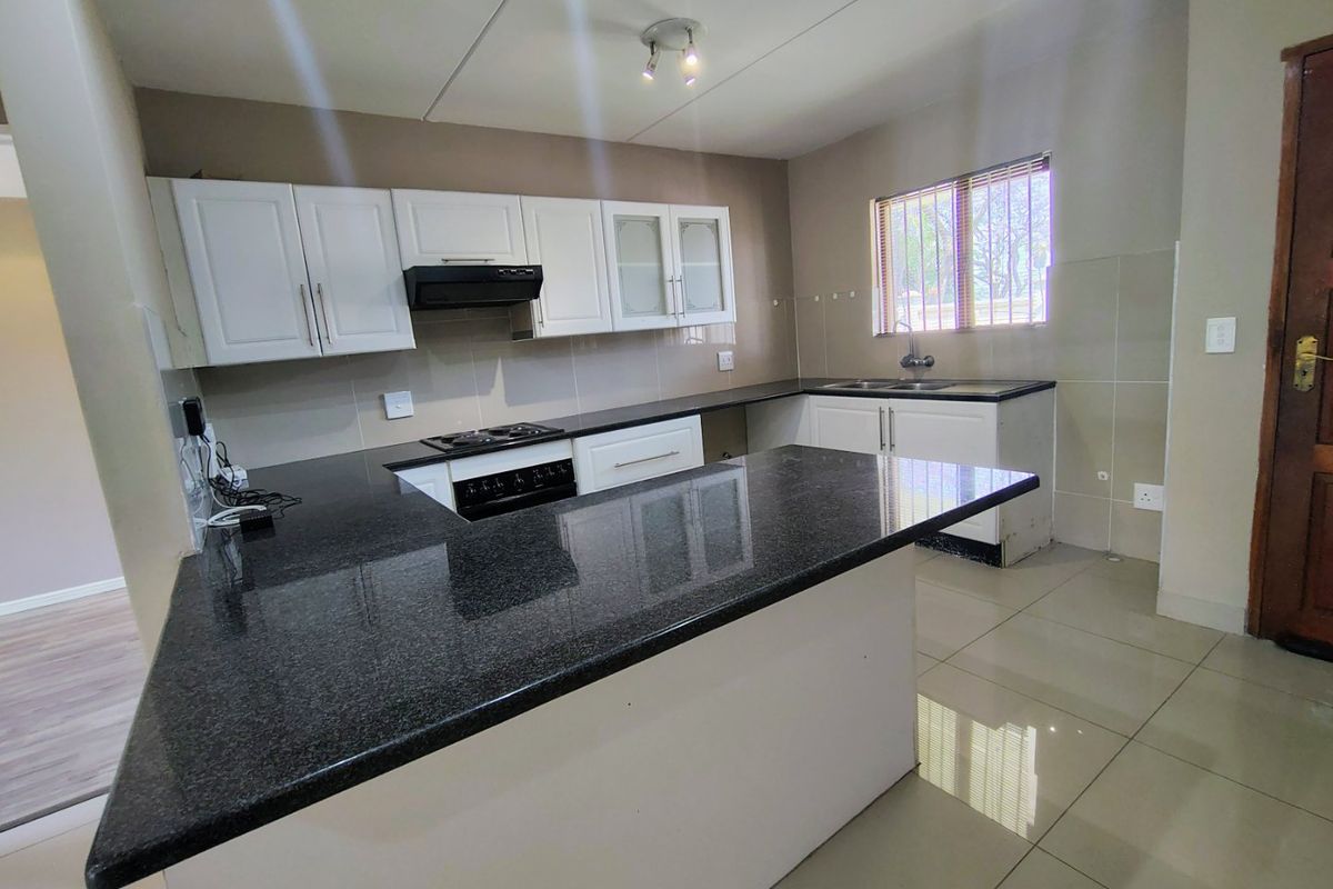 A clean, functional kitchen featuring granite countertops, built-in cabinetry, an electric hob with extractor, and tiled flooring throughout.