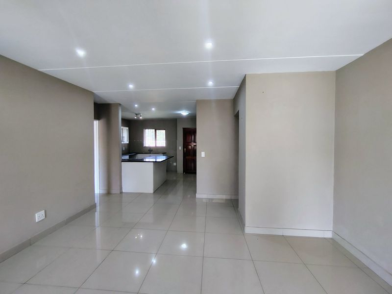 Spacious open-plan living area featuring neutral tiled flooring, recessed downlights, and a functional kitchen with a breakfast island.