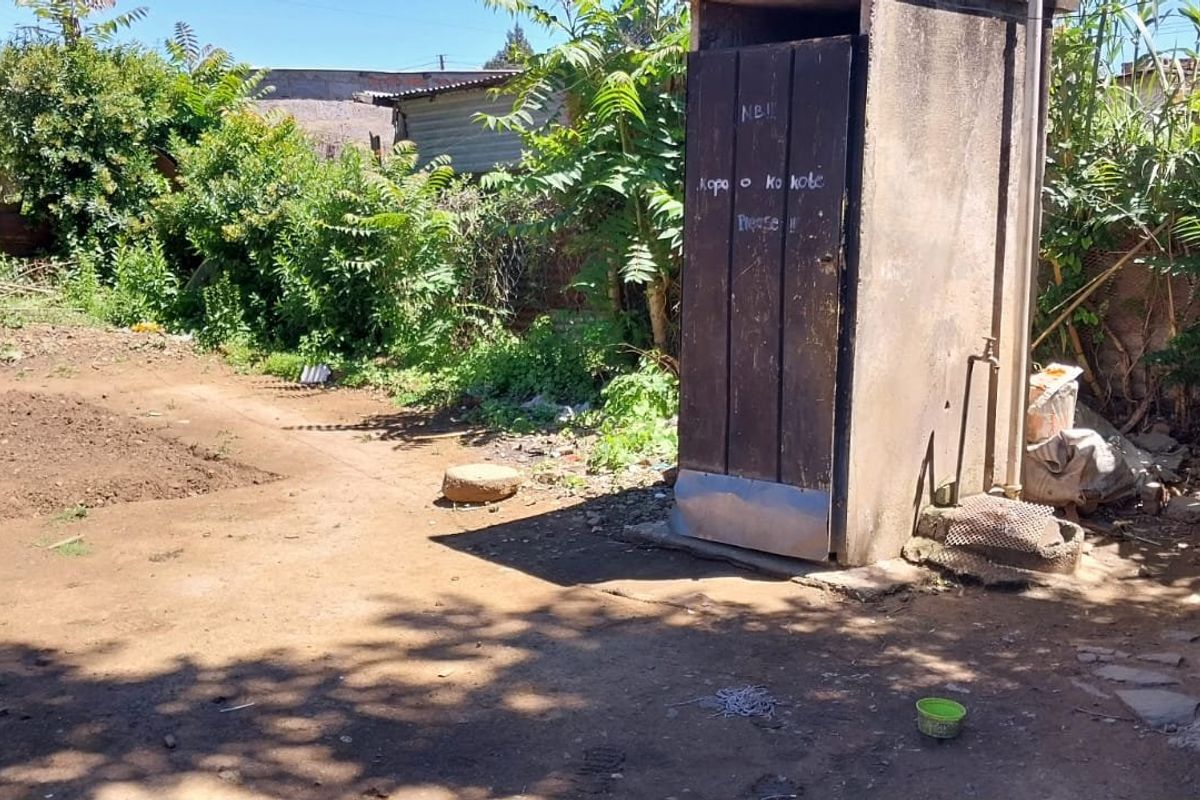 A view of the rear yard featuring an outdoor toilet structure and exposed brickwork, requiring significant maintenance and landscaping.