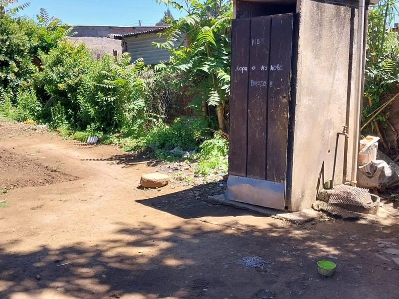 A view of the rear yard featuring an outdoor toilet structure and exposed brickwork, requiring significant maintenance and landscaping.