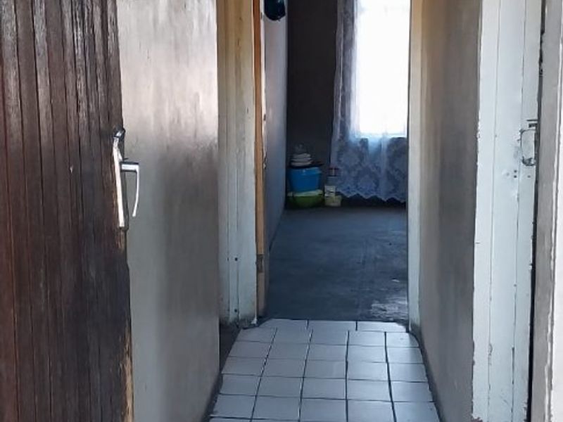A narrow interior hallway featuring tiled flooring, showing signs of wear including damaged tiles and peeling paint on the walls and ceiling.