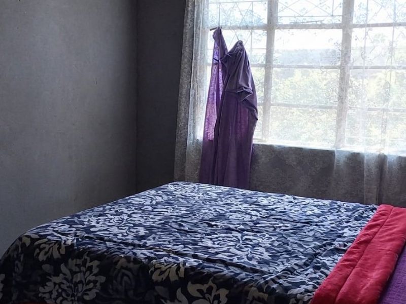 A bedroom featuring a window with security bars and significant ceiling damage requiring repair and renovation.
