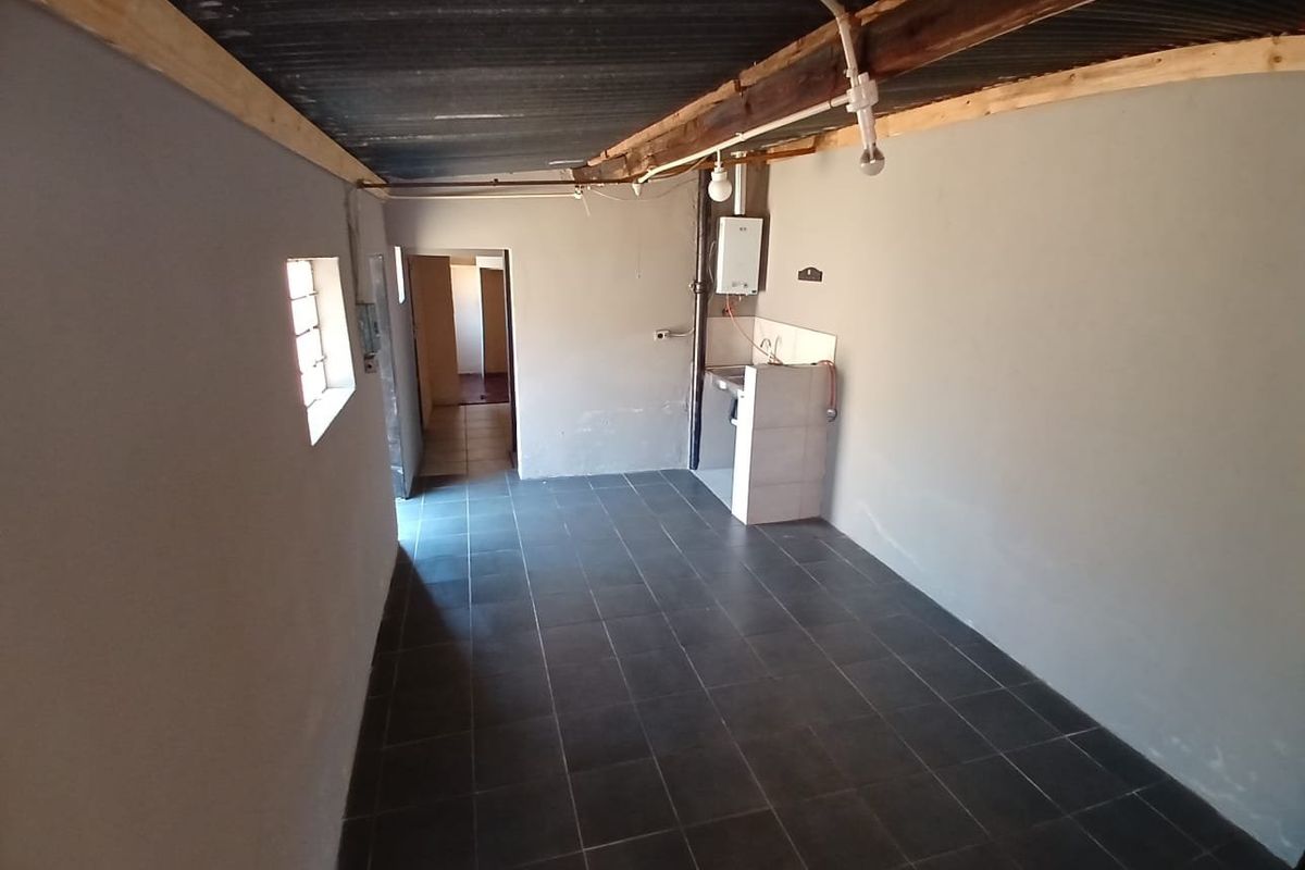 A basic, unfinished kitchen area featuring tiled flooring, a simple tiled sink counter, and exposed ceiling structure, offering potential for renovation.