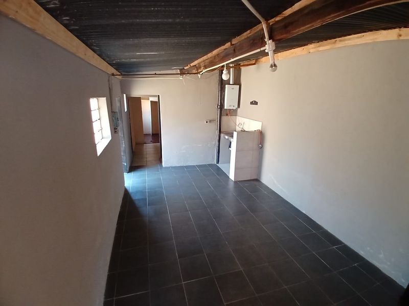 A basic, unfinished kitchen area featuring tiled flooring, a simple tiled sink counter, and exposed ceiling structure, offering potential for renovation.