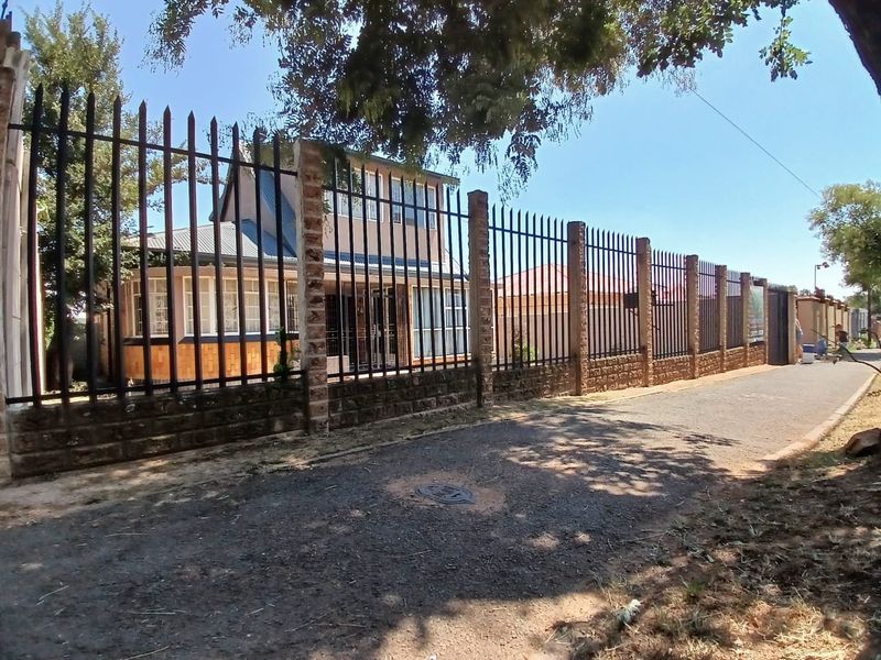 Street view of the property featuring a long metal security fence with brick pillars and a view of the house facade.