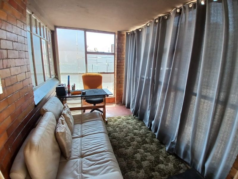 Enclosed sunroom or balcony featuring exposed brick walls and large windows, offering a versatile space that could be updated for modern use.