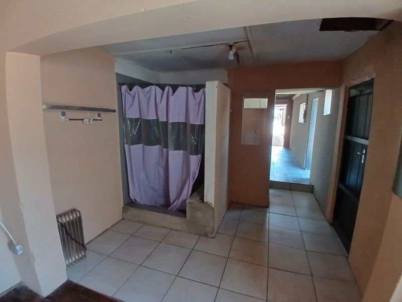A basic bathroom area featuring tiled flooring and a shower cubicle, currently in need of renovation and cosmetic repairs to the ceiling and walls.