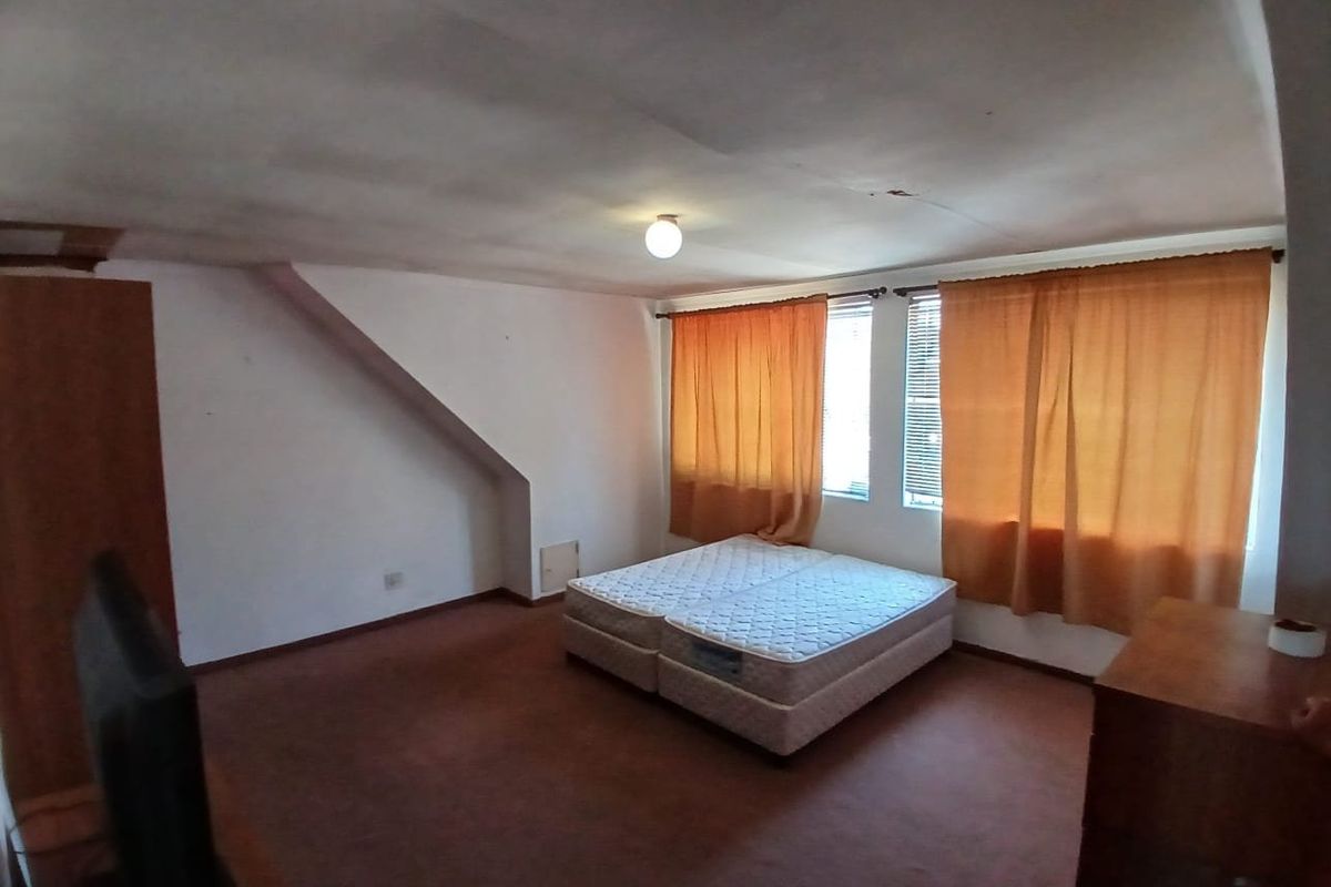 A bedroom featuring a sloped ceiling, built-in cupboard, and carpeted flooring. The room requires cosmetic updates to improve its overall condition.