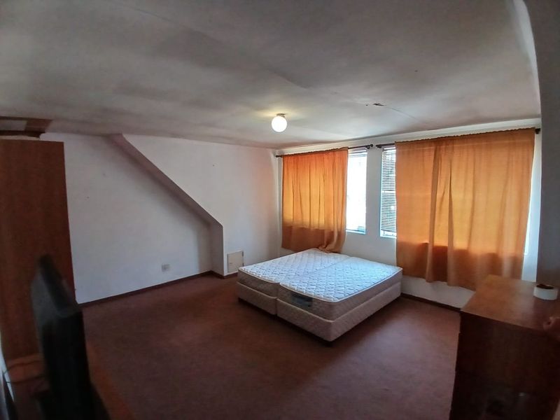 A bedroom featuring a sloped ceiling, built-in cupboard, and carpeted flooring. The room requires cosmetic updates to improve its overall condition.