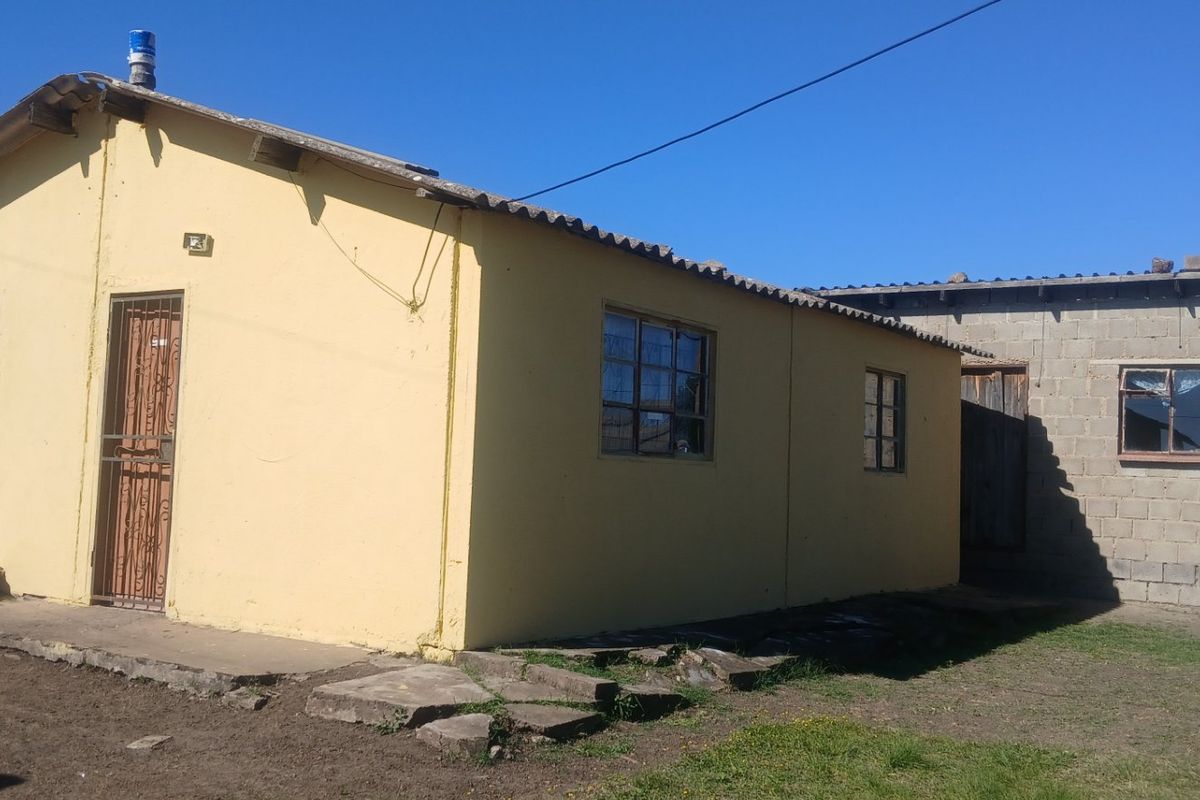 Rear view of a detached house featuring a yellow painted main structure and an adjacent unfinished concrete block extension.