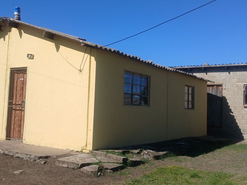 Rear view of a detached house featuring a yellow painted main structure and an adjacent unfinished concrete block extension.