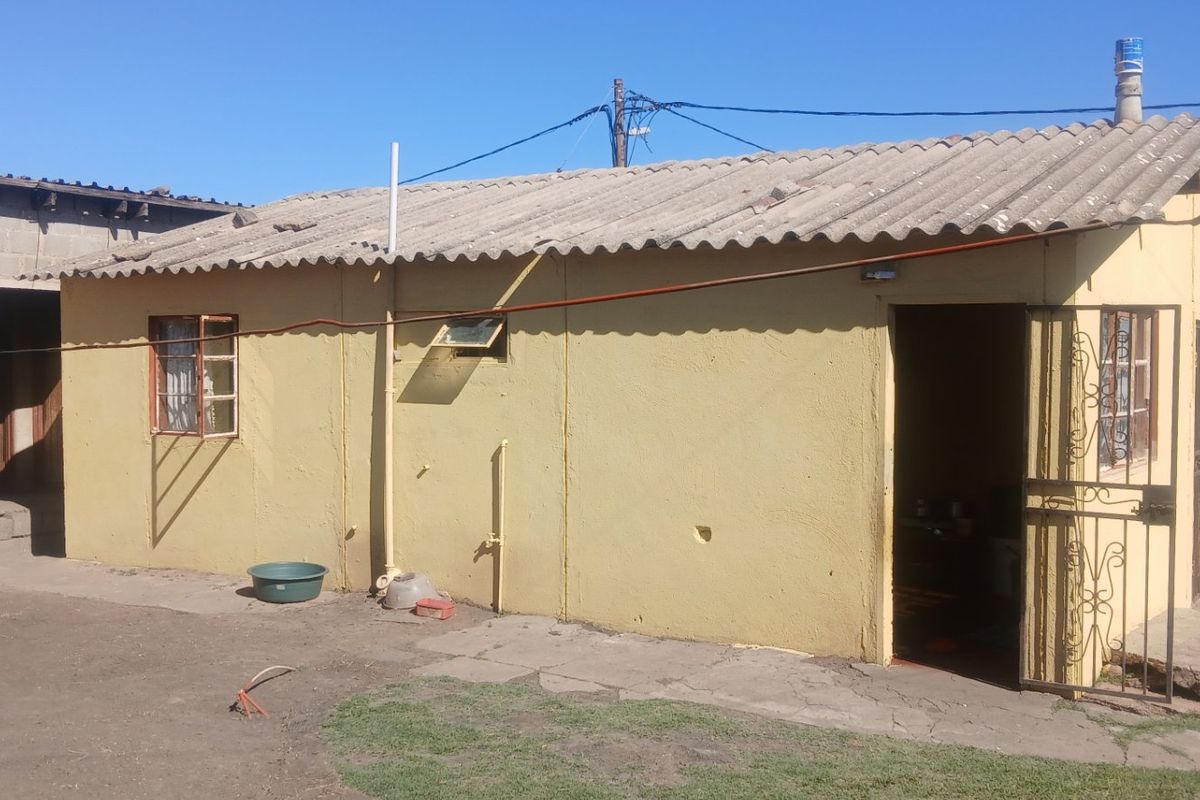Rear view of a single-story house featuring a corrugated roof, yellow painted exterior walls, and a security gate entrance.