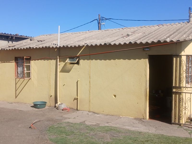 Rear view of a single-story house featuring a corrugated roof, yellow painted exterior walls, and a security gate entrance.