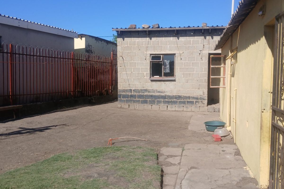 A rear yard area featuring a concrete block outbuilding, metal security fencing with razor wire, and a paved walkway leading to the main structure.