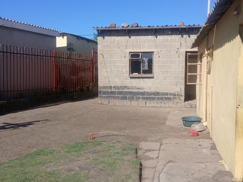 A rear yard area featuring a concrete block outbuilding, metal security fencing with razor wire, and a paved walkway leading to the main structure.