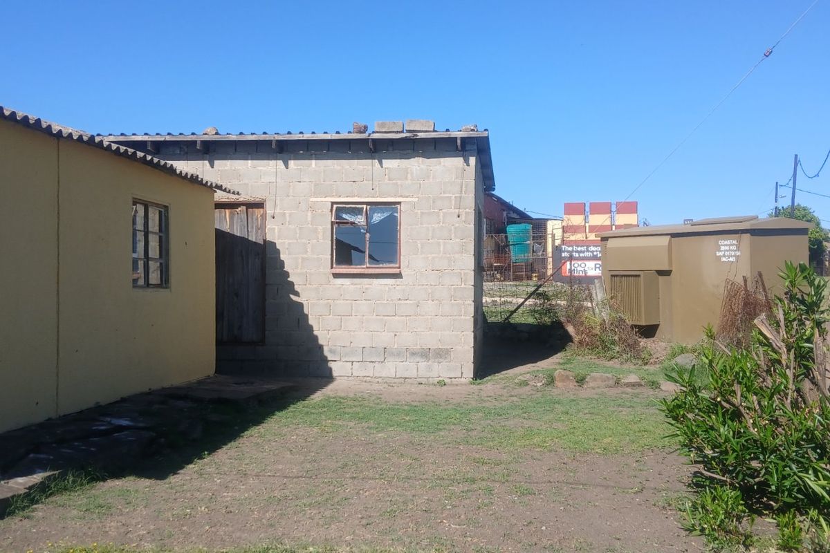 Rear exterior view of the property showing a concrete block structure and a yellow painted wall with steel frame windows.
