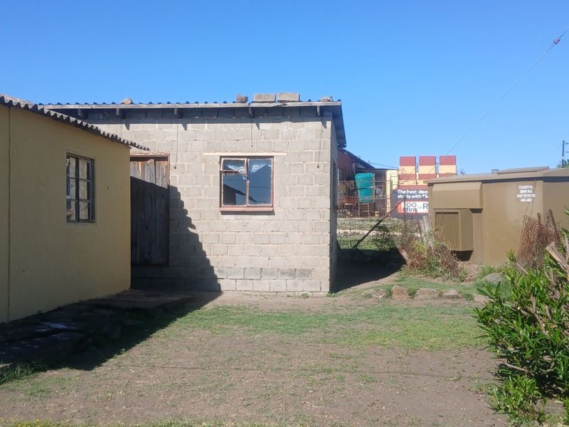 Rear exterior view of the property showing a concrete block structure and a yellow painted wall with steel frame windows.