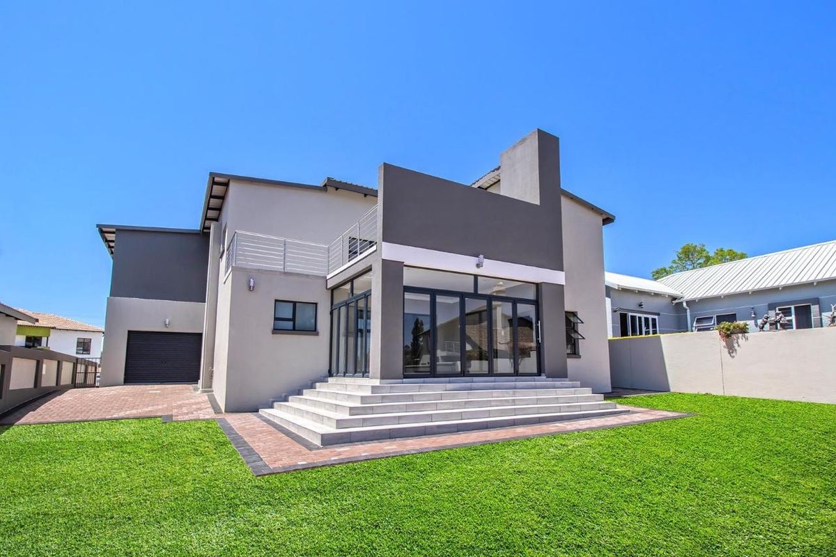 Rear view of a modern two-story house featuring a paved patio, concrete steps, bi-fold glass doors, and an upper-level balcony.