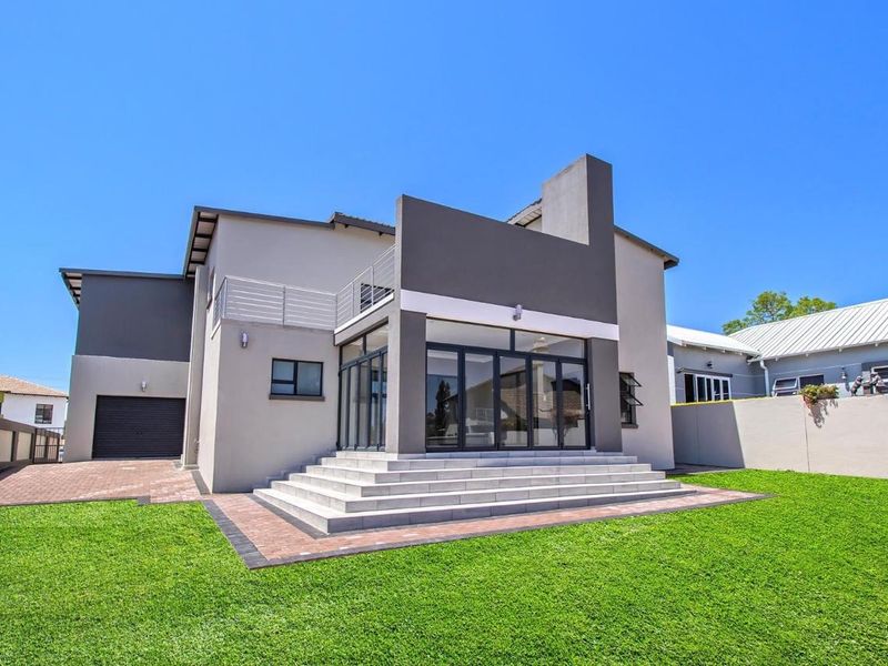 Rear view of a modern two-story house featuring a paved patio, concrete steps, bi-fold glass doors, and an upper-level balcony.