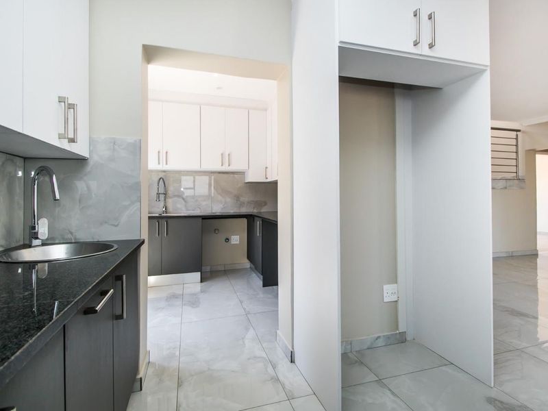A clean, modern scullery featuring sleek cabinetry, granite countertops, a stainless steel sink, and dedicated space for a refrigerator.