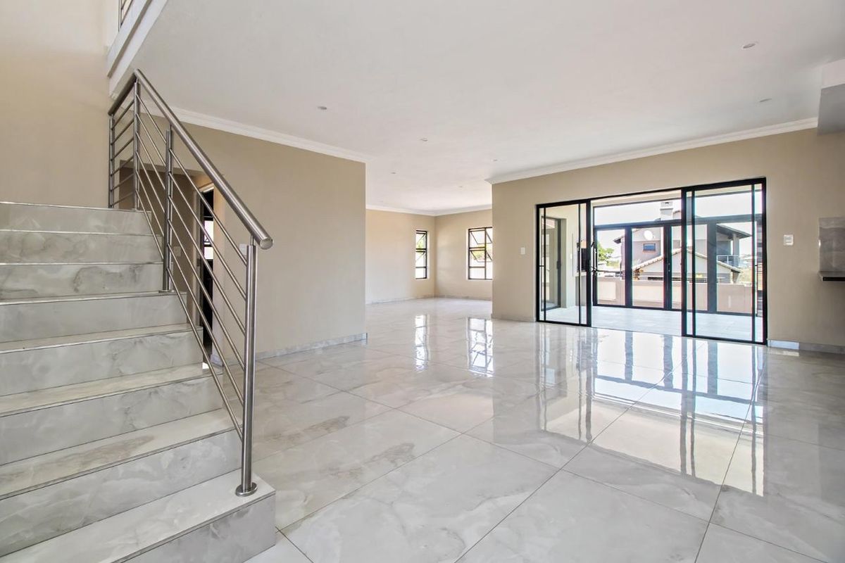 Spacious open-plan living area featuring polished marble-look floor tiles, a modern stainless steel staircase, and large sliding glass doors leading to an outdoor patio.