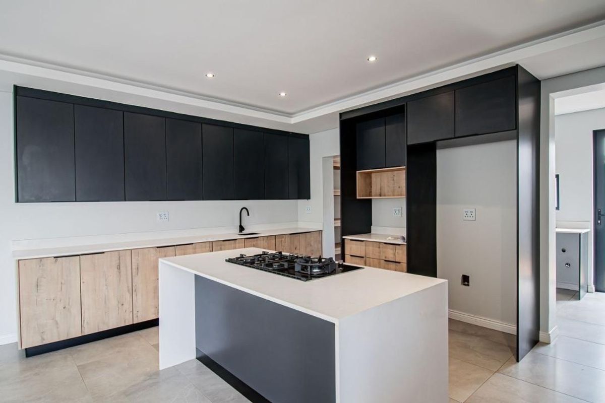 Modern kitchen featuring two-tone cabinetry, a central island with a gas hob, stone countertops, and sleek tiled flooring in an open-plan layout.