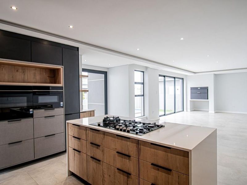 Modern open-plan kitchen and living area featuring a central island with gas hob, sleek cabinetry, recessed lighting, and large sliding doors leading outdoors.
