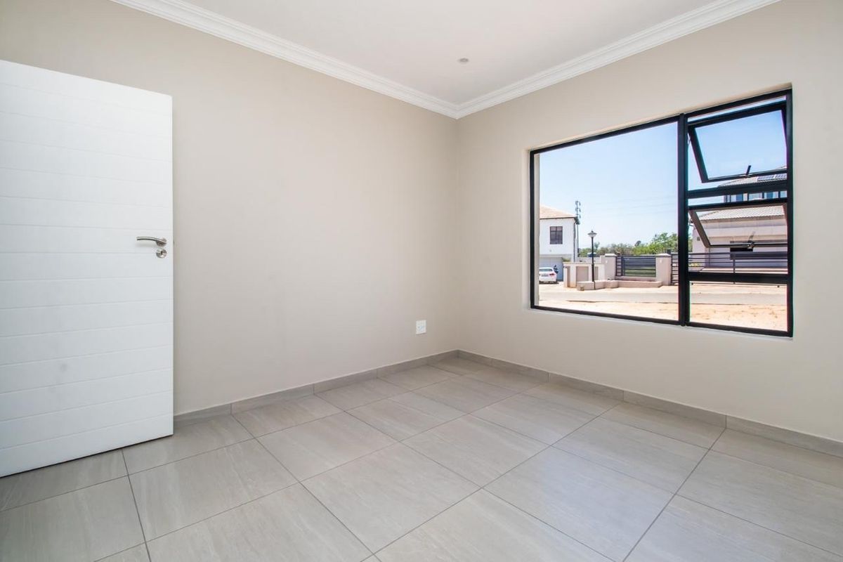 A bright, empty bedroom featuring neutral tiled flooring, modern black aluminium window frames, and clean finishes, ready for personalization.