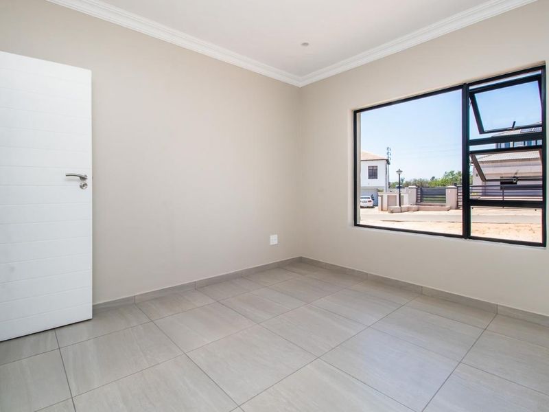A bright, empty bedroom featuring neutral tiled flooring, modern black aluminium window frames, and clean finishes, ready for personalization.