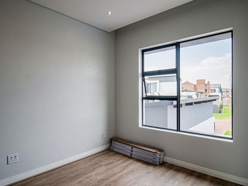 A bright, modern, and empty bedroom featuring laminate flooring, neutral walls, and a large aluminium-framed window with a view of the surrounding neighbourhood.