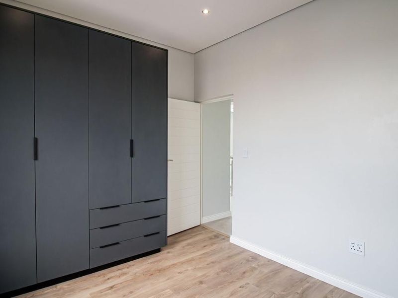 A clean, modern bedroom featuring dark grey built-in cupboards, light wood-look laminate flooring, and neutral wall finishes.